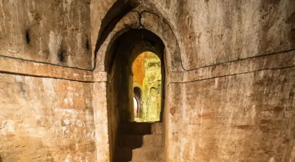 Un antico passaggio conduce ai **Bologna canali sotterranei**. Scale di pietra scendono nell'oscurità, tra muri di mattoni e archi in mattoni.