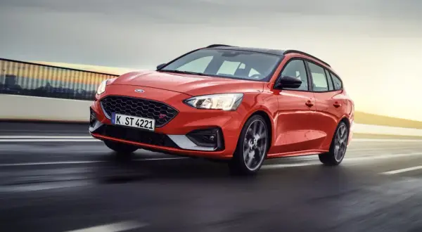 Czerwony Ford Focus sedan ST pędzi po drodze, z rozmytym tłem sugerującym dużą prędkość.