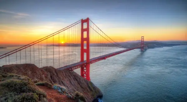 Zachód słońca nad Zatoką San Francisco, gdzie majestatyczny san francisco most rozciąga się nad wodą, a jego czerwone wieże lśnią w złotym świetle.