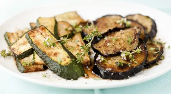 Gebratene zucchini und aubergine in der pfanne, garniert mit frischen Kräutern.
