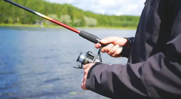 Mann hält Angelrute und Rolle am See. Perfekter Ort, wo kann ich angeln?