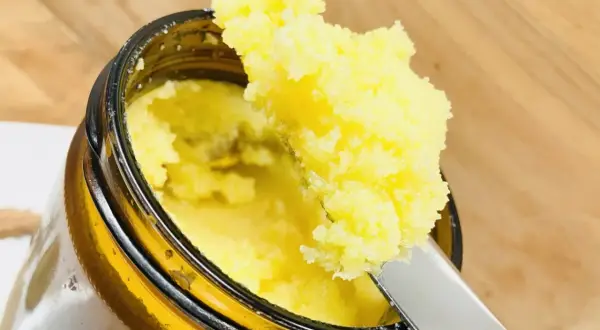 Ein Löffel hebt goldgelbes Ghee Butter aus einem Glas. Was ist Ghee Butter? Ein geklärte Butter, ideal zum Kochen.