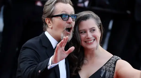 Gary Oldman z żoną, uśmiechnięci i pełni życia, pozują do zdjęć na czerwonym dywanie.