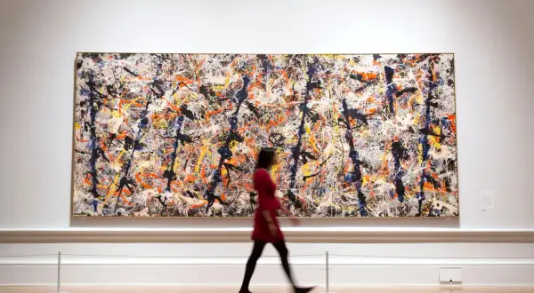 A woman in a red dress walks past a large, vibrant canvas of contemporary abstract expressionism, a masterpiece of splattered paint.