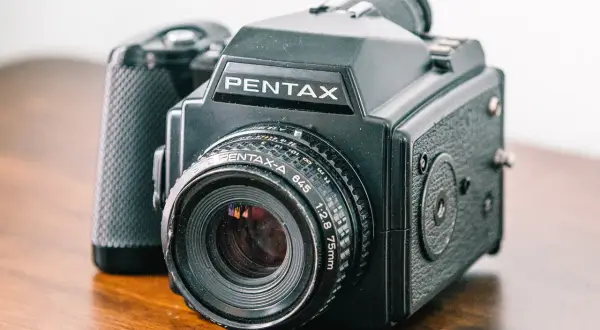A black Pentax 645 medium format point and shoot camera with a 75mm lens sits on a wooden surface.
