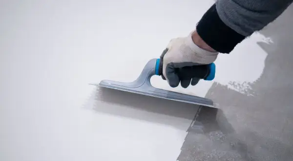 Mano con guanto stende resina, mostrando la differenza tra resina epossidica e poliuretanica per pavimenti.