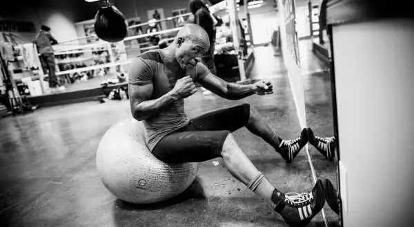 A determined Hopkins boxer, sweat glistening, trains on a stability ball in a boxing gym.