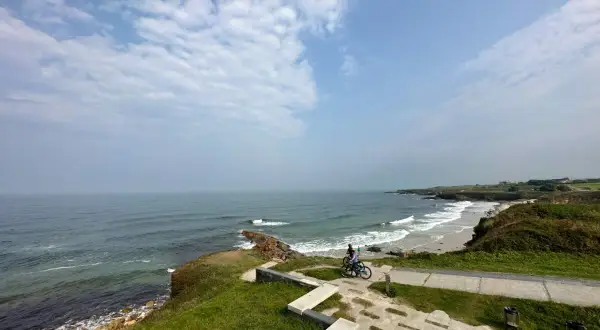 Un paseo en bicicleta por las **playas cerca de Foz**, con el mar Cantábrico de fondo y un cielo nublado.