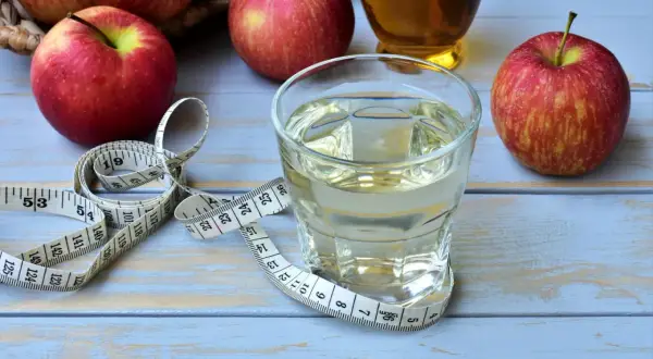 Ein Glas Apfelessig, Äpfel und ein Maßband. Ein täglicher Apfelessig-Schluck für die Gesundheit und eine schlanke Linie.
