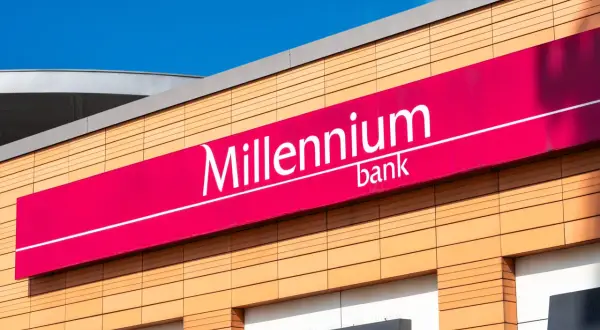 Elegancki budynek z logo Millennium bank. Jasne panele elewacyjne i fuksjowy baner z nazwą banku.