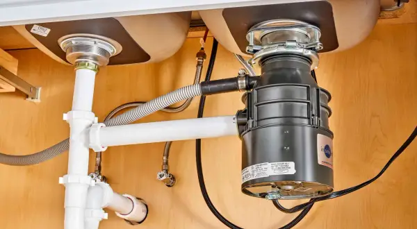 Under-sink plumbing with a garbage disposal installed, showing pipes and connections. This image illustrates how to install a garbage disposal.
