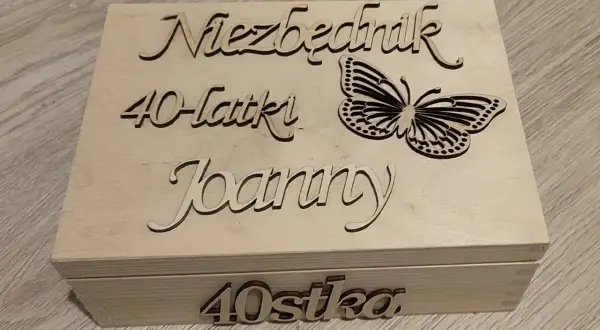 Drewniana skrzynka z napisem "Niezbędnik 40-latki Joanny" i motylem. Na froncie "40stka".