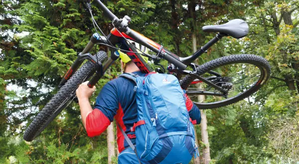 Mann mit Mountainbike und Deuter Trans Alpine 24 Rucksack im Wald.