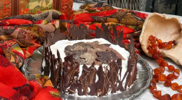 A chocolate-decorated cake with whipped cream and chocolate leaves on top, set on a silver platter.