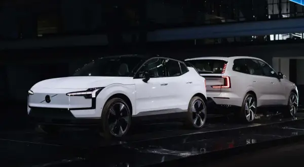 Dwa białe, nowe Volvo na czarnej scenie. Jedno z przodu z charakterystycznymi światłami, drugie z tyłu z nowoczesnymi lampami.