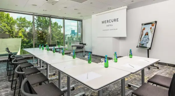 Sala konferencyjna w hotelu Mercure Poznań Centrum. Długi stół, krzesła, projektor i logo hotelu.