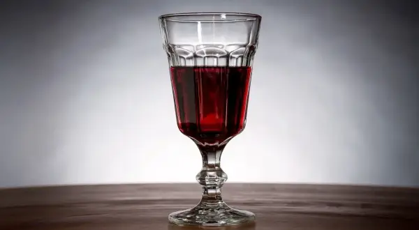 Szklanka z ciemnoczerwonym winem z jeżyn, stojąca na drewnianym blacie.