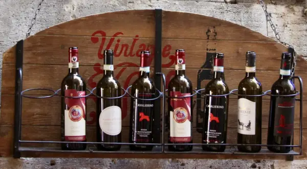 Rząd butelek wina, w tym Chianti Classico, na drewnianym stojaku z napisem "Vintage". Idealne na podróż po regionie Toskania.