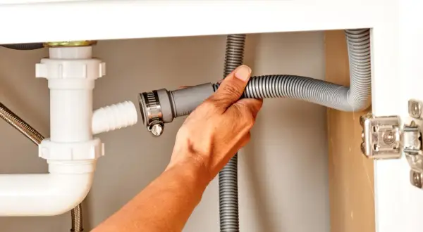 Hand connecting a dishwasher drain hose to a sink drain pipe.