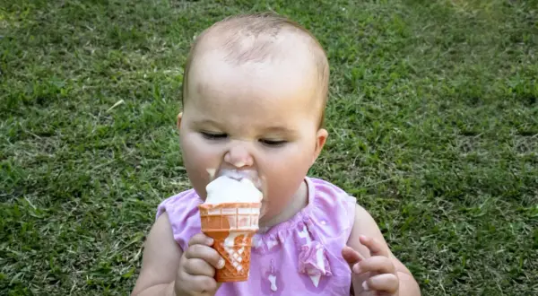 Kleines Baby mit Eiscreme im Gras. Ab wann Eis baby? Diese süße Erfahrung beginnt oft, wenn die Kleinen neugierig werden.