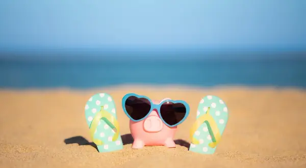Świnka skarbonka w okularach przeciwsłonecznych i klapki na plaży. To symbol oszczędzania na wakacje ZUS.