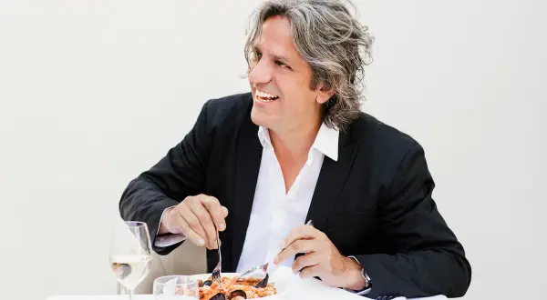 Giorgio Locatelli, chef stellato Michelin, sorride mentre gusta un piatto di pesce.