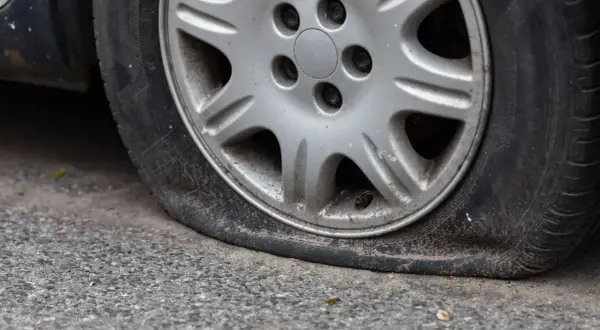 Gros plan sur une roue de voiture avec un pneu dégonflé, posée sur un trottoir gris. La jante est en alliage argenté.