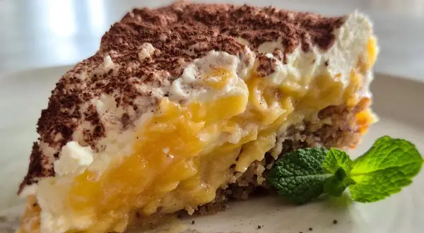 Ein saftiger Apfelkuchen-Schnitte mit cremiger Füllung, Kakao bestäubt und Minze garniert.