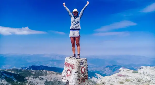 Szczyt Korab zdobyty! Radosna turystka z rękami w górze na skale z napisem "KORAB" i wysokością 2764 m.