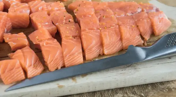 Świeży, pokrojony w kostkę i plastry łosoś, idealny jako jaki łosoś do sushi, leży na desce obok noża.