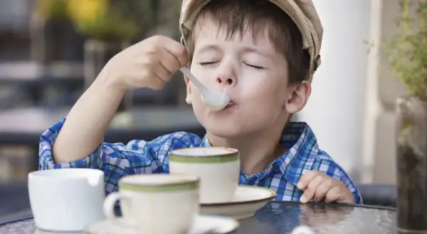 Bambino con cappellino gustando un delizioso cappuccino senza caffè, con gli occhi chiusi per il piacere.