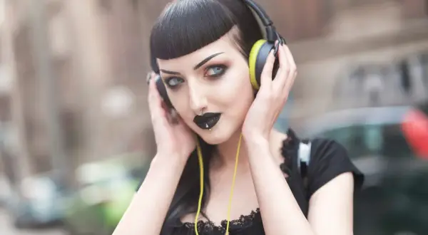 Mroczna goth girl w słuchawkach, z czarną szminką i kolczykiem w nosie, słucha muzyki na ulicy.