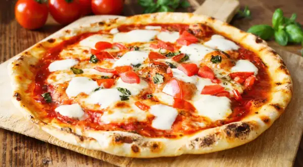Pyszne ciasto na pizzę bez wyrastania, z pomidorami, mozzarellą i bazylią, na drewnianej desce.