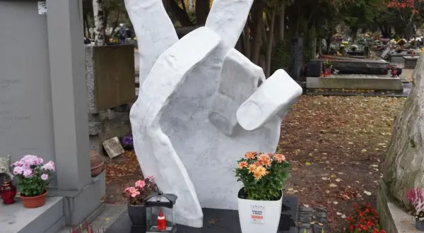 Monumentalna dłoń z symbolem pokoju na tle cmentarza. Wiele nagrobków tworzy ten zadumany zespół.