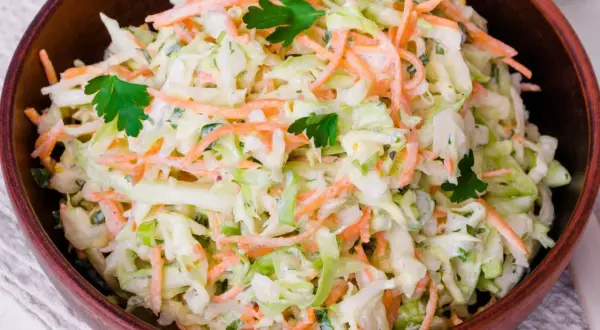 Klasyczny coleslaw w drewnianej misce, pełen chrupiącej kapusty i marchewki, udekorowany natką pietruszki.