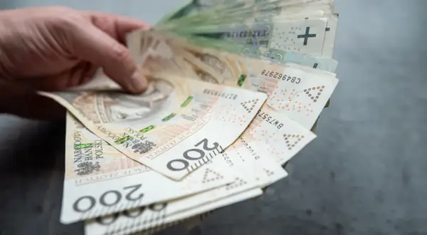 Dłoń trzyma plik banknotów 200 zł. Czy współwłaściciel konta może wypłacić pieniądze po śmierci właściciela?