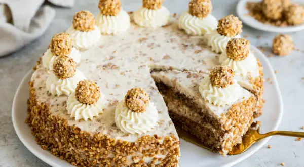 Eine köstliche Giotto Torte, verziert mit Sahnetuffs und Haselnusskugeln, umgeben von gehackten Nüssen.