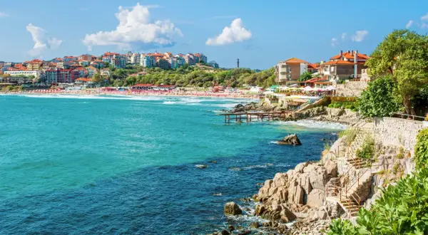 Słoneczne wybrzeże z turkusowym morzem, plażą pełną ludzi i kolorowymi budynkami na wzgórzu – tak z czego słynie Bułgaria.