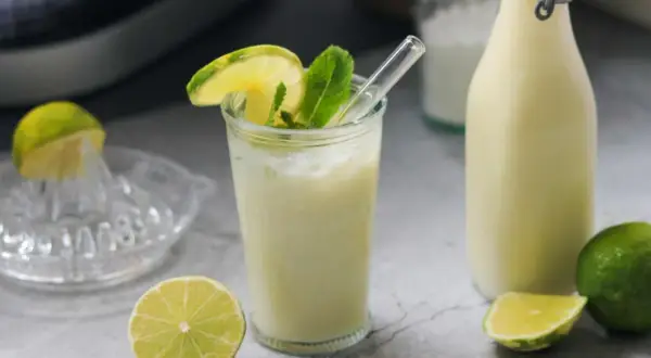 Erfrischende brasilianische Limonade mit Limettenscheiben und Minze, daneben eine Flasche und frische Limetten.