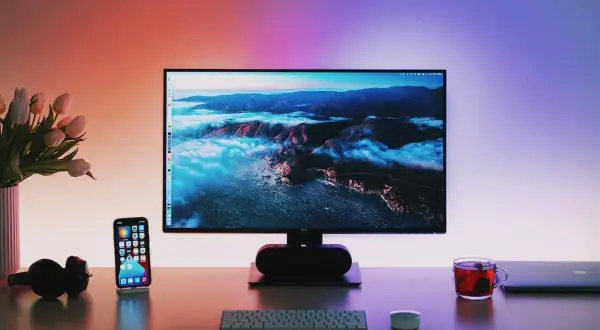 Biurko z monitorem wyświetlającym krajobraz, telefonem, słuchawkami i kubkiem herbaty.