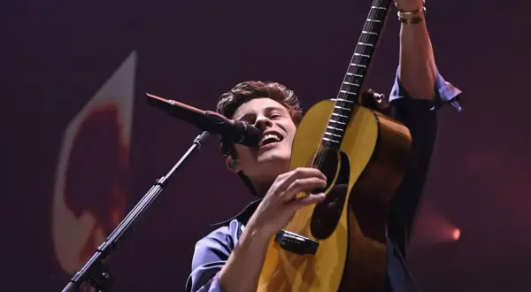 Shawn Mendes śpiewa i gra na gitarze na koncercie.