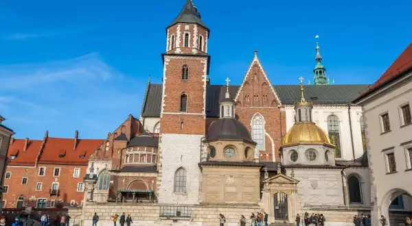 Majestatyczna katedra wawelska z cegły i kamienia, z dominującą wieżą i złotą kopułą, na tle błękitnego nieba.