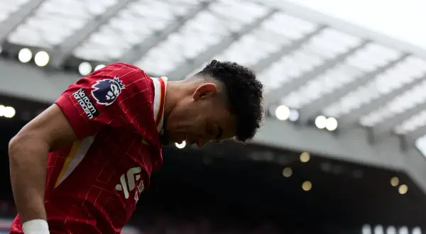 Piłkarz w czerwonej koszulce Liverpoolu z opuszczoną głową, na tle trybun stadionu.
