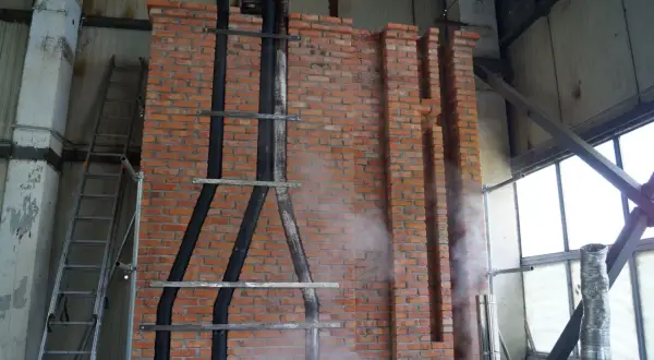 Instalacja wkładu kominowego do starego komina: czarne rury prowadzone po ceglanej ścianie, drabina, para wodna.