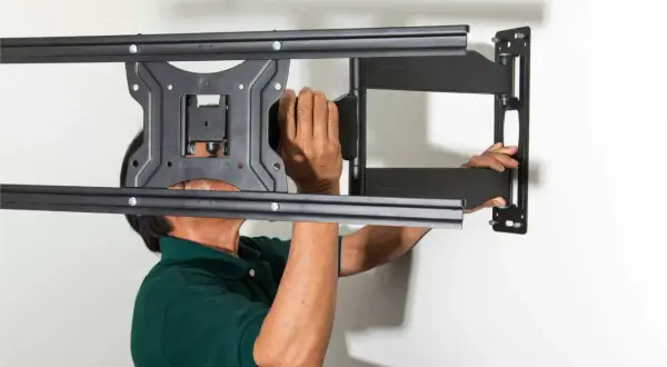Man in green shirt mounting a TV bracket to the wall.
