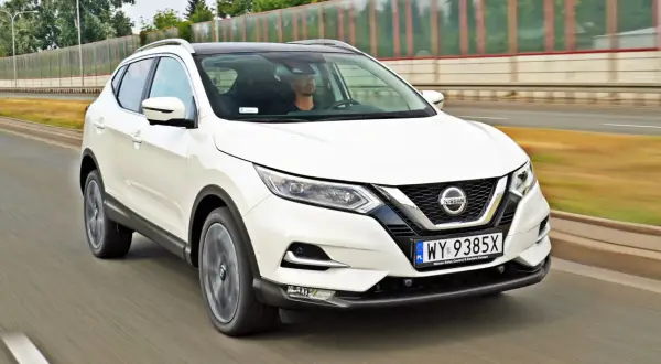 Biały Nissan Qashqai jedzie po drodze. Sprawdź aktualną nissan qashqai cena i oferty.