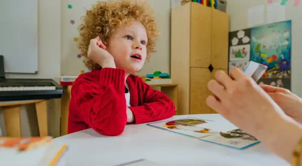 Chłopiec z kręconymi włosami, u którego zdiagnozowano orzeczenie Asperger, uczy się z kart obrazkowych.
