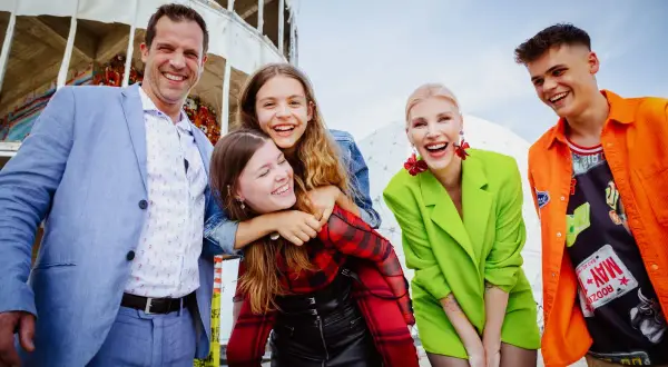 Eine fröhliche Familie genießt den Tag in Berlin. Vater, Mutter und drei Kinder lachen ausgelassen vor einer futuristischen Kulisse.