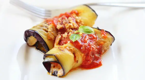 Deliziosi involtini di melanzane alla siciliana, ripieni e conditi con sugo rosso e basilico fresco, pronti per essere gustati.