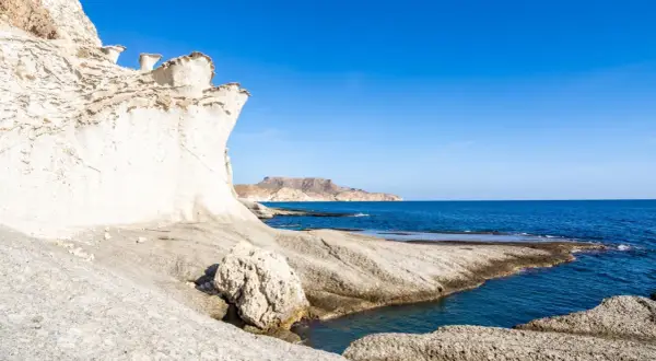 Formaciones rocosas blancas y erosionadas en una cala blanca Almería, con el mar azul intenso y montañas al fondo.